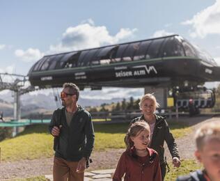 Eine Familie mit zwei Kindern auf der Seiser Alm, im Hintergrund ein Sessellift