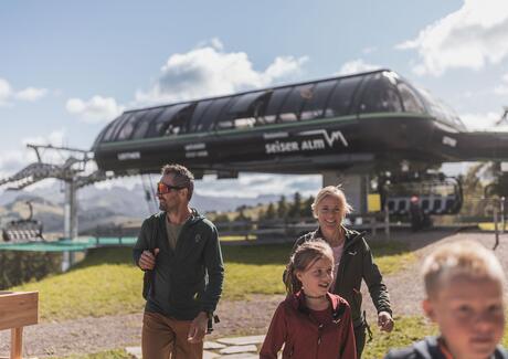 Eine Familie mit zwei Kindern auf der Seiser Alm, im Hintergrund ein Sessellift