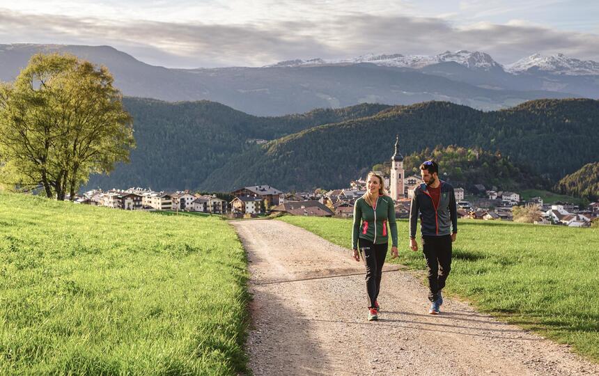 Ein Mann und eine Frau spazieren, während im Hintergrund Kastelruth zu sehen ist