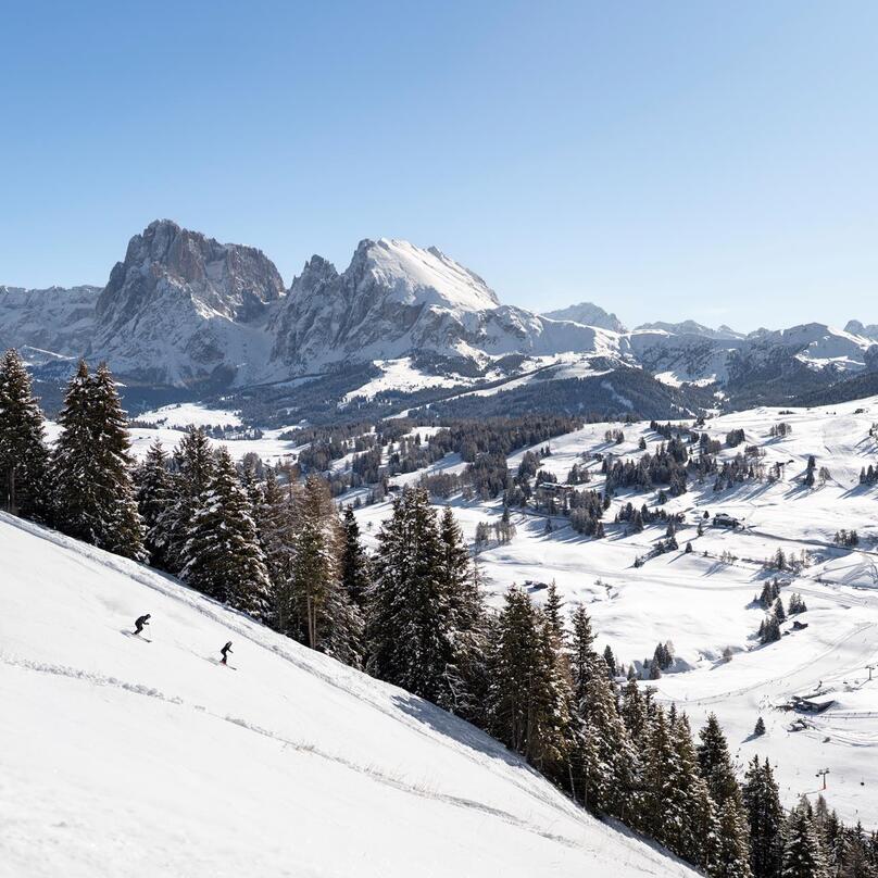 A man and a woman ski down a slope