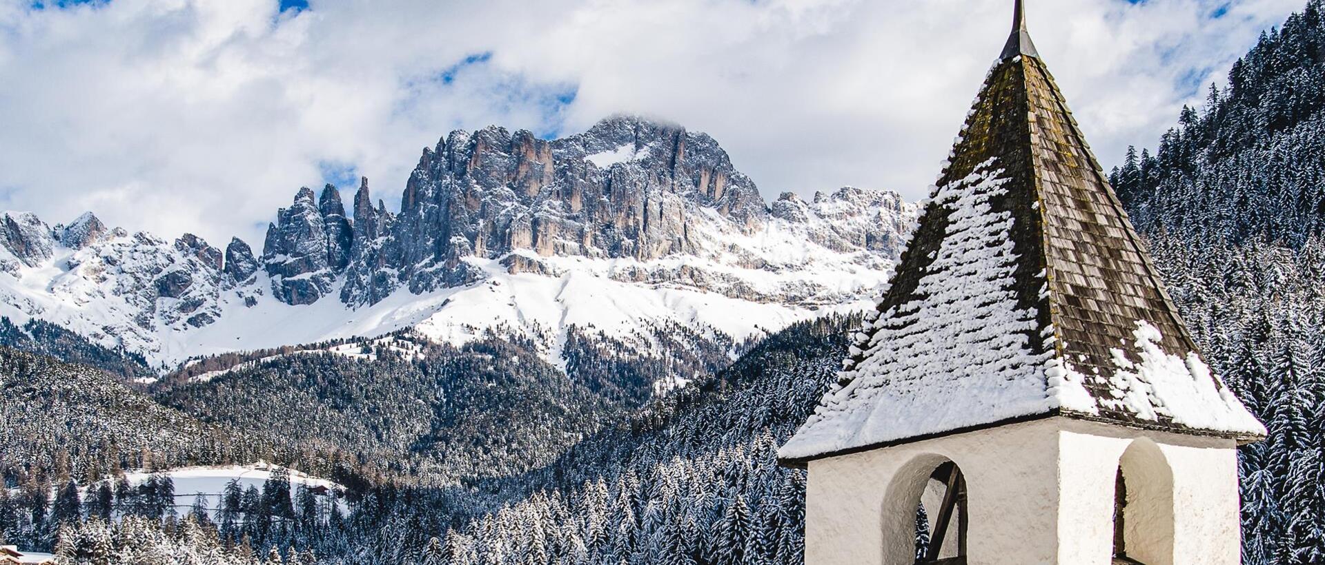 Der Kirchturm von Tiers am Rosengarten; im Hintergrund der Rosengarten, schneebedeckt