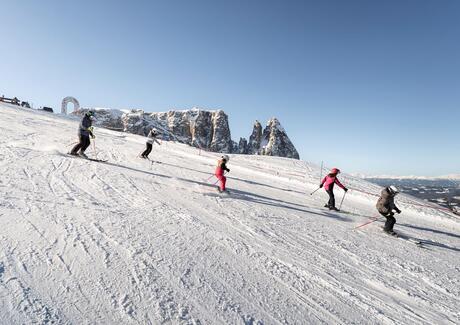 Eine Familie fährt Ski, im Hintergrund sieht man den Schlern
