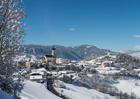 Ein Mann und eine Frau sitzen auf einer Holzbank und blicken auf Völs am Schlern