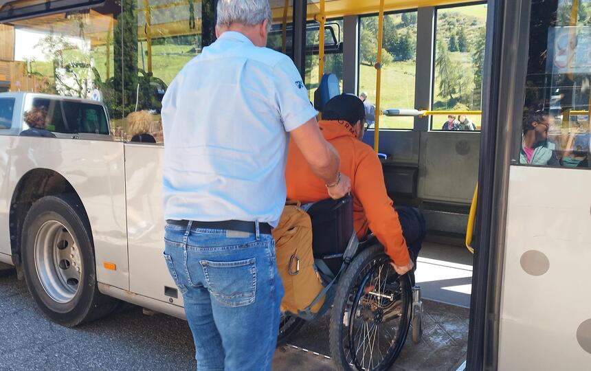 Ein Mann hilft einem Mann im Rollstuhl beim Einsteigen in einen Bus