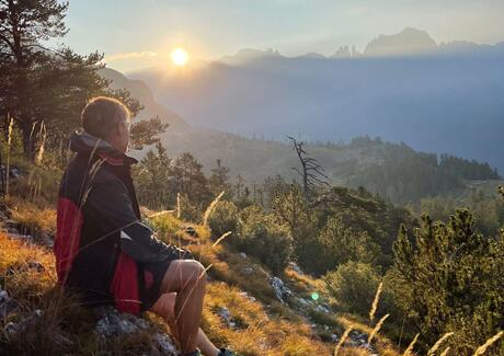 Un uomo è seduto su una montagna e osserva il tramonto