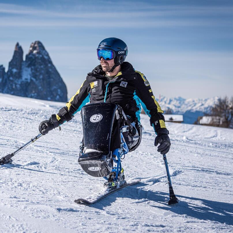 Ein Skifahrer fährt über eine verschneite Skipiste in einer alpinen Berglandschaft