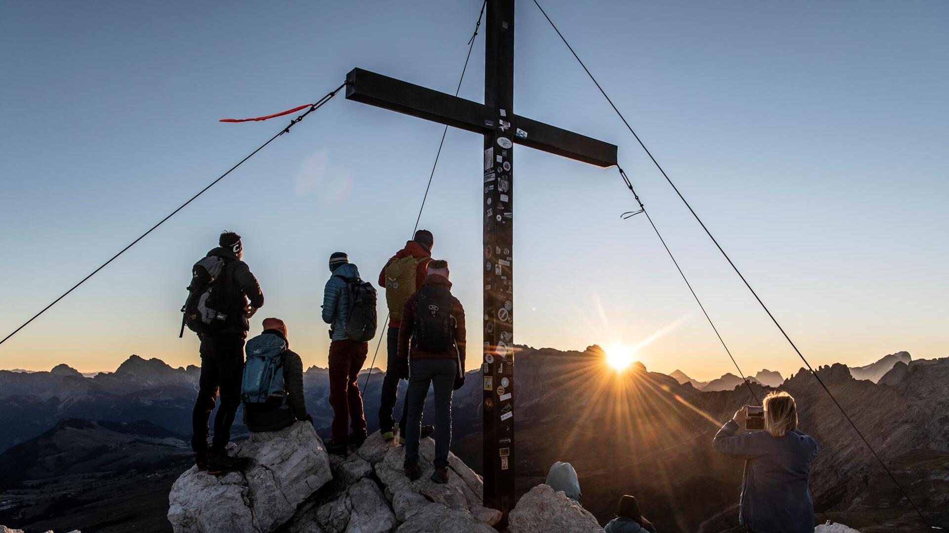 Un gruppo di persone si trova su una cima di montagna all’alba