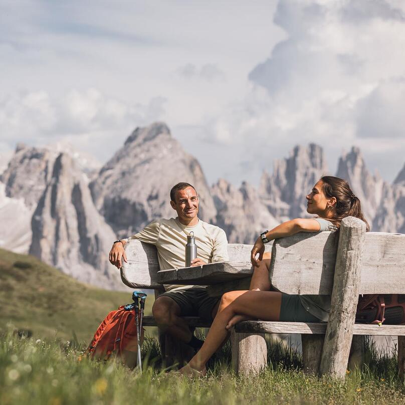 Ein Mann und eine Frau sitzen auf einer Holzbank mit Blick auf die Dolomiten