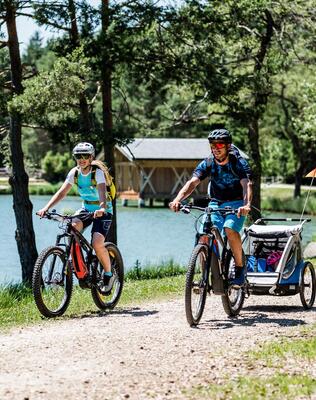 Eine Familie fährt am Völser Weiher entlang