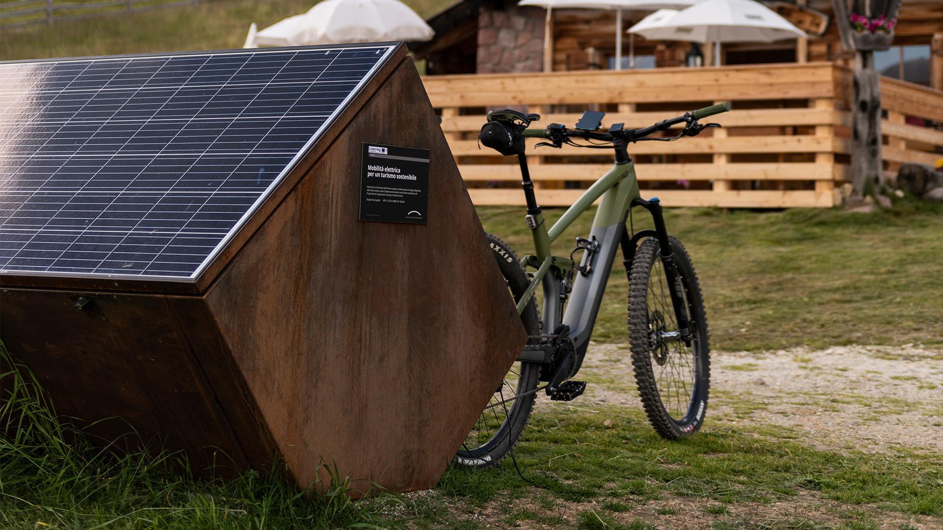 Ein E-bike lädt an einer mobilen Zapfsäule vor einer Almhütte