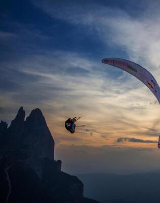 Ein Mann fliegt mit dem Gleitschirm; im Hintergrund ist der Schlern bei Sonnenuntergang zu sehen